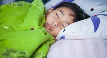 Healthy child. Little asian boy sleeping peacefully on bed in dark bedroom.
